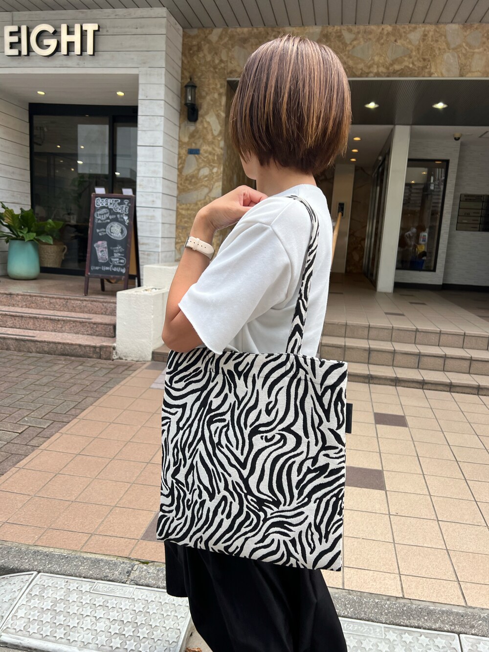 ホワイト系のトートバッグ、ブラック系のスカート、ホワイト系のトップスを着用したレディースの夏コーディネートの2枚目の写真