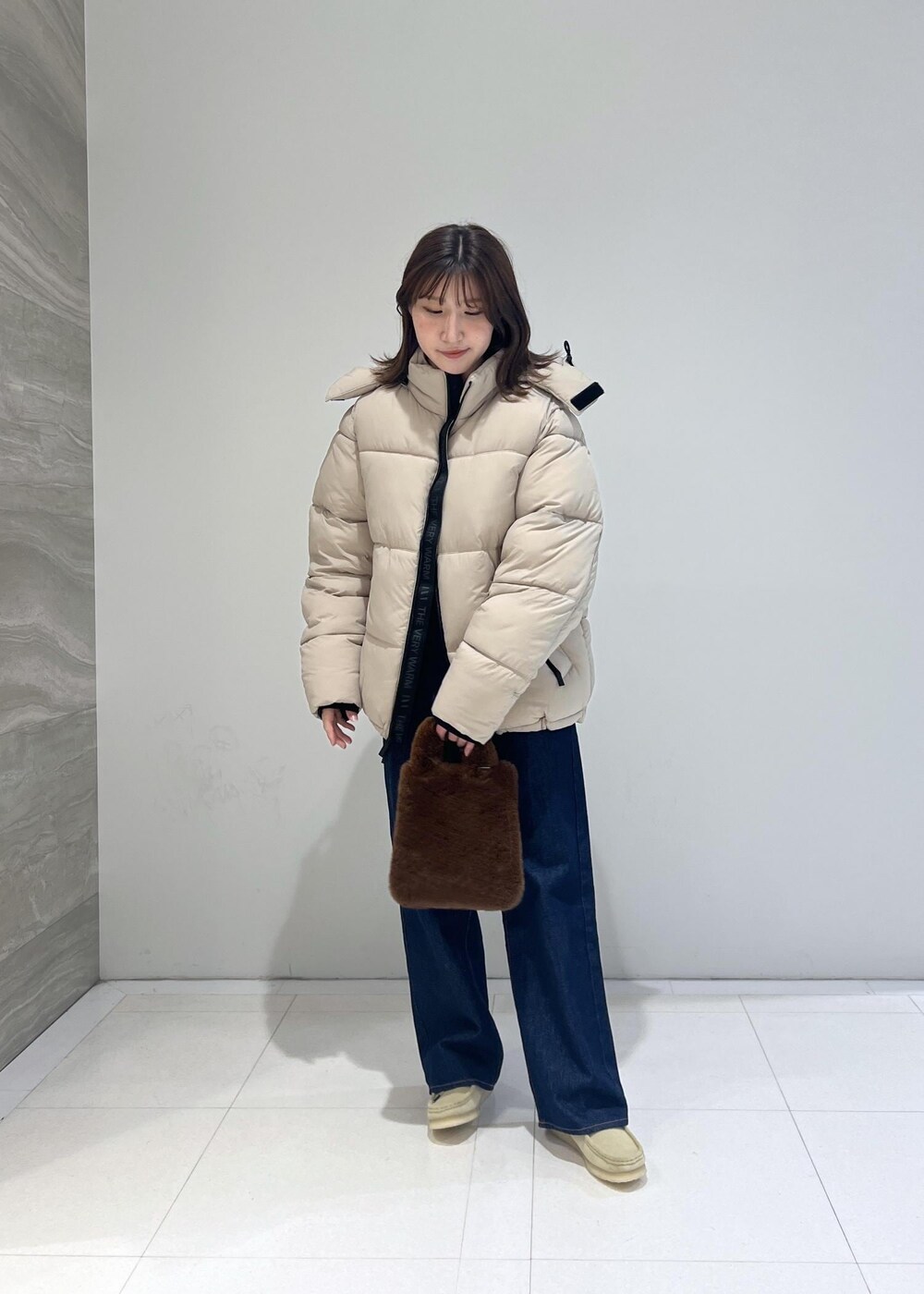 ブルー系のデニムパンツ、ベージュ系のダウンジャケット/コート、ベージュ系のモカシン/デッキシューズを着用したレディースの秋コーディネートの2枚目の写真