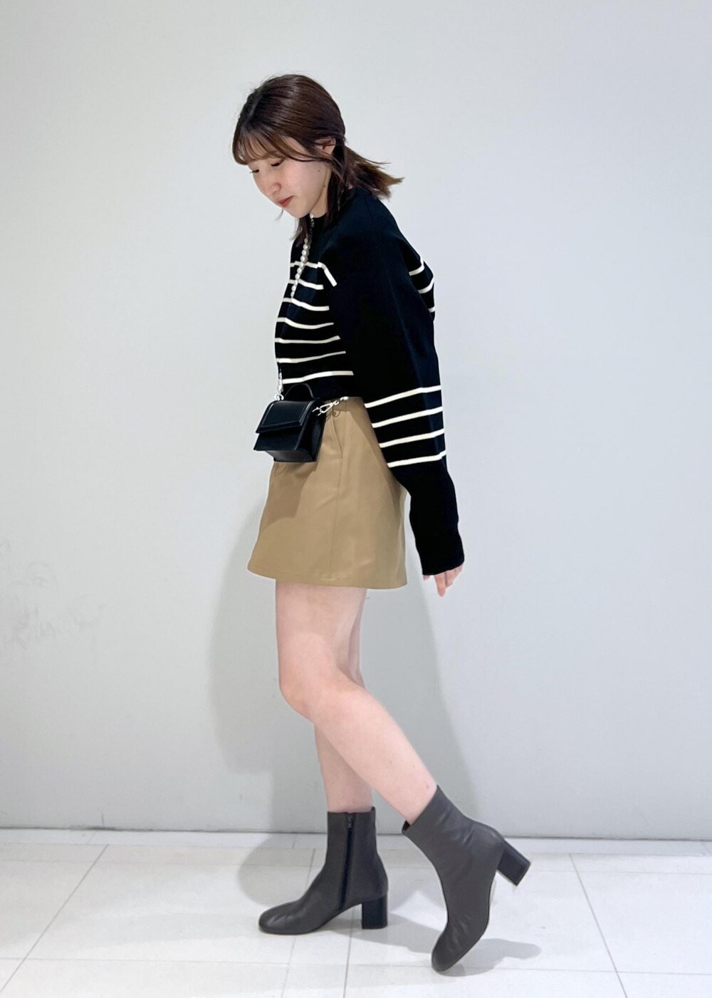ブラック系のニット/セーター、ブラック系のショルダーバッグ、ベージュ系のスカートを着用したレディースの秋コーディネートの2枚目の写真
