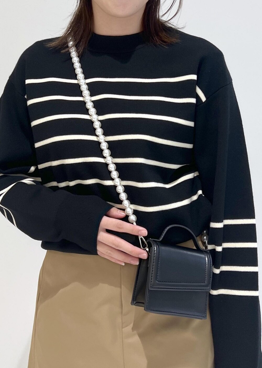 ブラック系のニット/セーター、ブラック系のショルダーバッグ、ベージュ系のスカートを着用したレディースの秋コーディネートの4枚目の写真