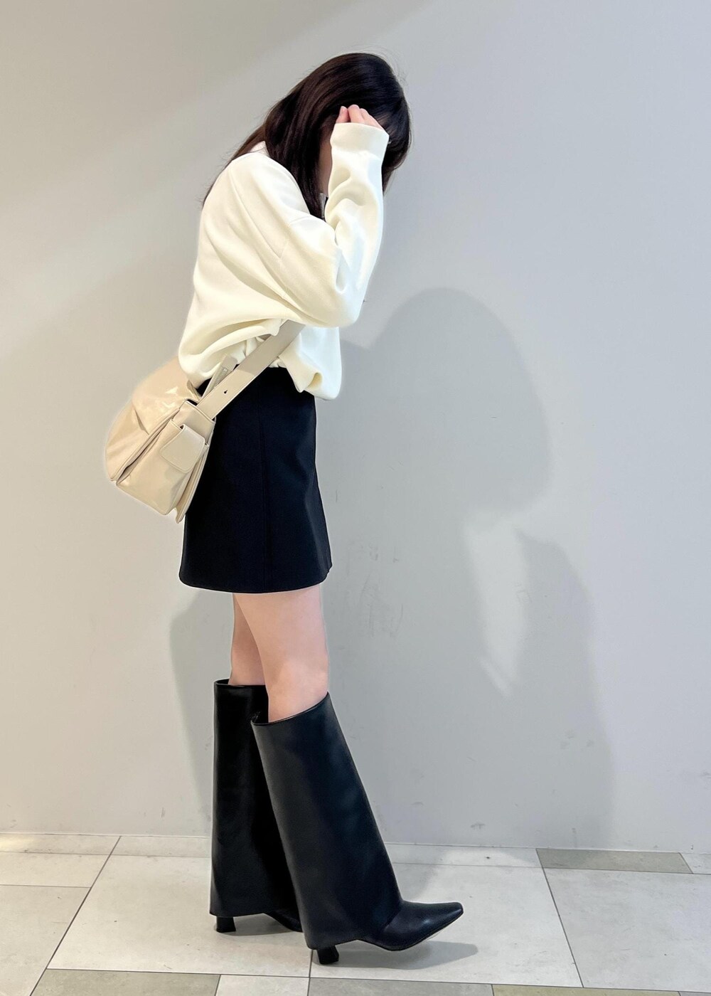 ブラック系のスカート、ベージュ系のショルダーバッグ、ホワイト系のニット/セーターを着用したレディースの冬コーディネートの2枚目の写真