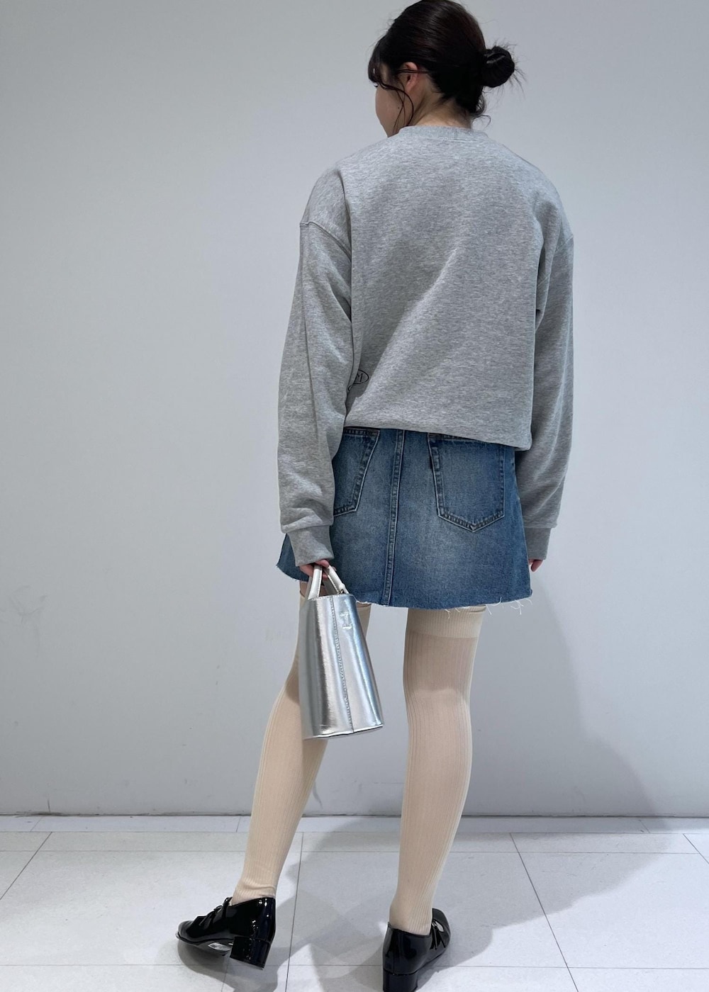 グレー系のスウェット、ブラック系のパンプス、ブルー系のデニムスカートを着用したレディースの冬コーディネートの2枚目の写真