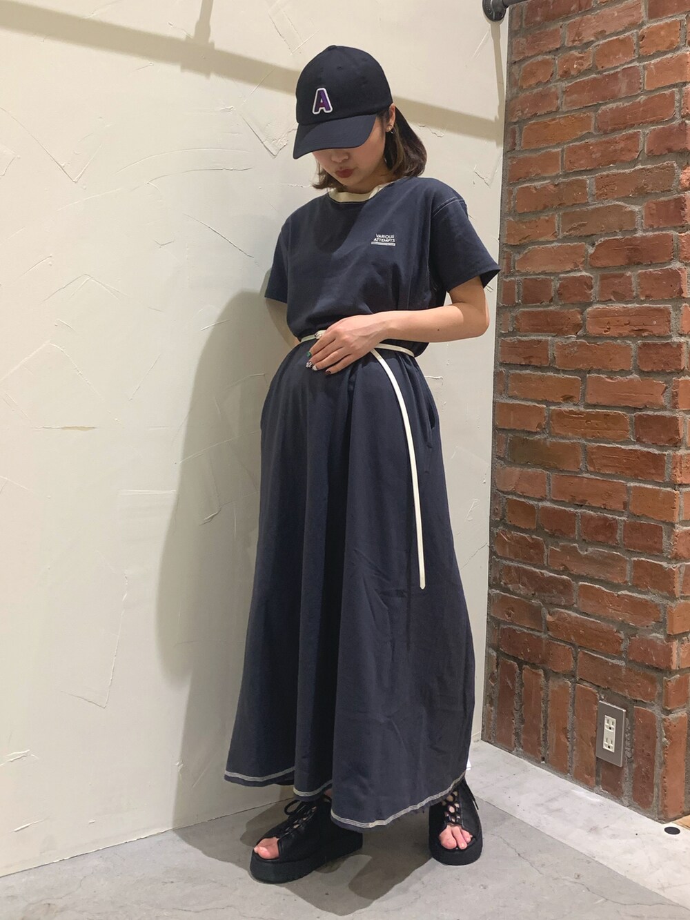 グレー系のワンピース、ブラック系のサンダル、ブラック系のキャップを着用したレディースの春コーディネートの2枚目の写真