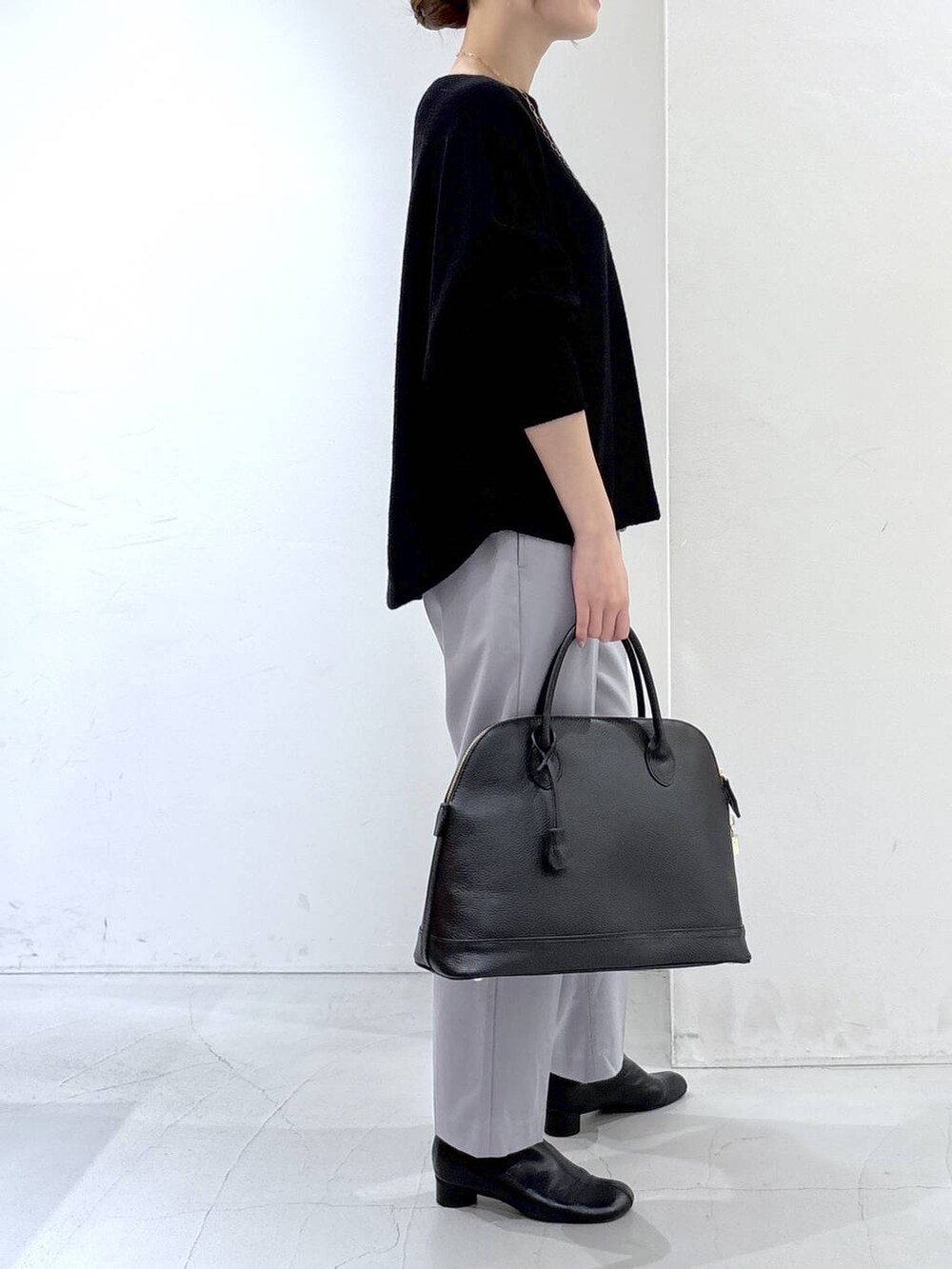 ブラック系のニット/セーター、ブラック系のボストンバッグ、グレー系のスラックスを着用したレディースの秋コーディネートの5枚目の写真