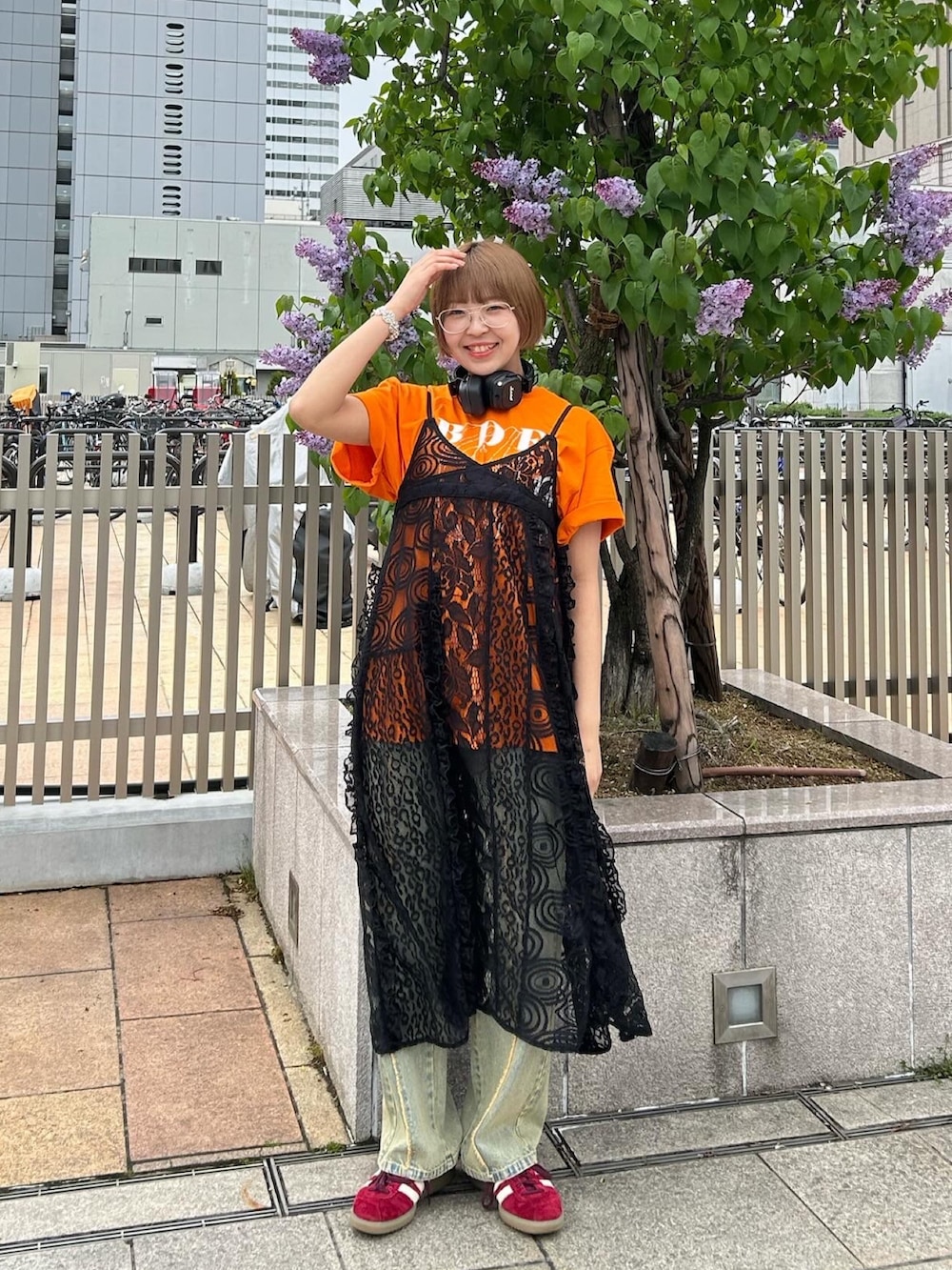 オレンジ系のTシャツ/カットソー、ブラック系のワンピース、ブルー系のデニムパンツを着用したレディースの春コーディネートの4枚目の写真