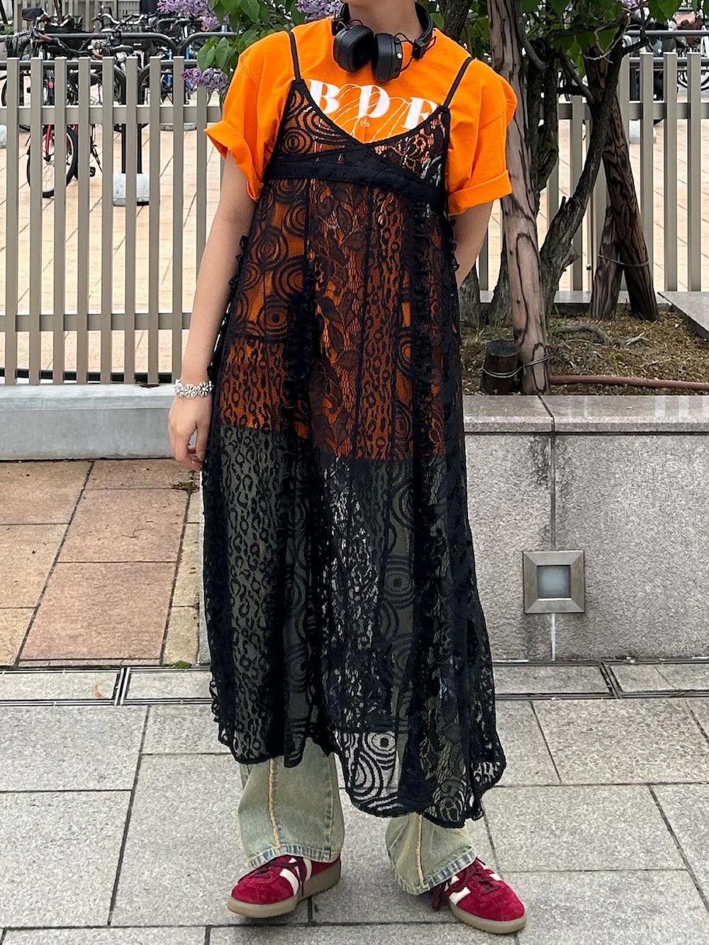 オレンジ系のTシャツ/カットソー、ブラック系のワンピース、ブルー系のデニムパンツを着用したレディースの春コーディネートの2枚目の写真