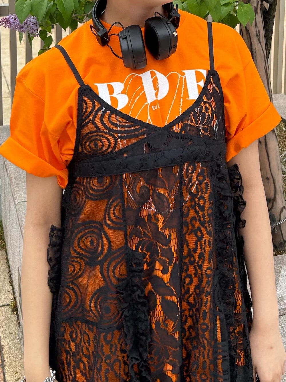 オレンジ系のTシャツ/カットソー、ブラック系のワンピース、ブルー系のデニムパンツを着用したレディースの春コーディネートの3枚目の写真