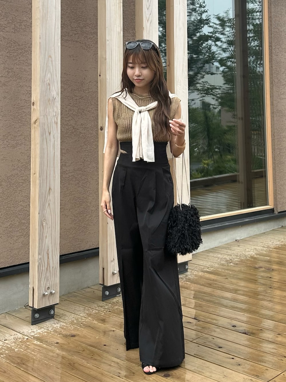 ブラック系のハンドバッグ、ブラック系のスラックス、ベージュ系のトップスを着用したレディースの夏コーディネートの2枚目の写真