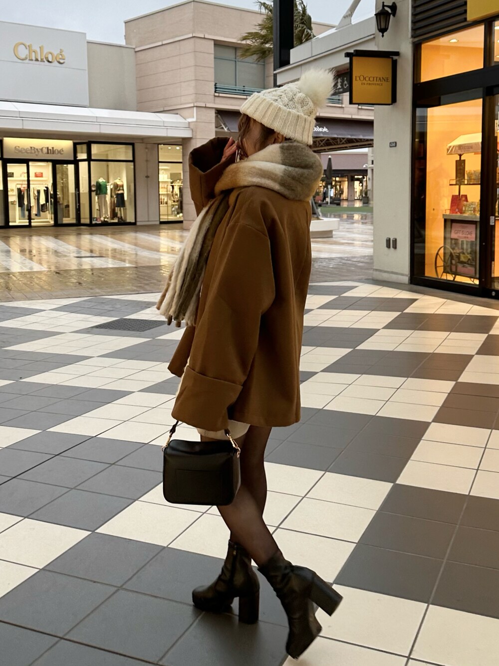 ブラック系のブーツ、ブラウン系のノーカラーコート、ブラック系のバッグを着用したレディースの冬コーディネートの2枚目の写真