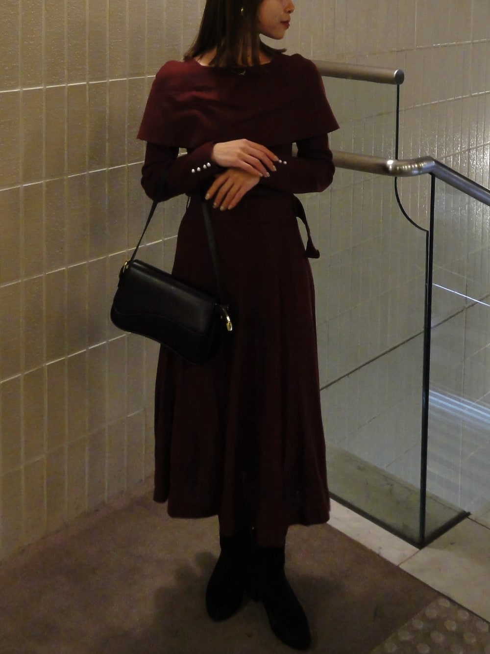 レッド系のワンピース、ブラック系のブーツ、ブラック系のバッグを着用したレディースの冬コーディネートの2枚目の写真