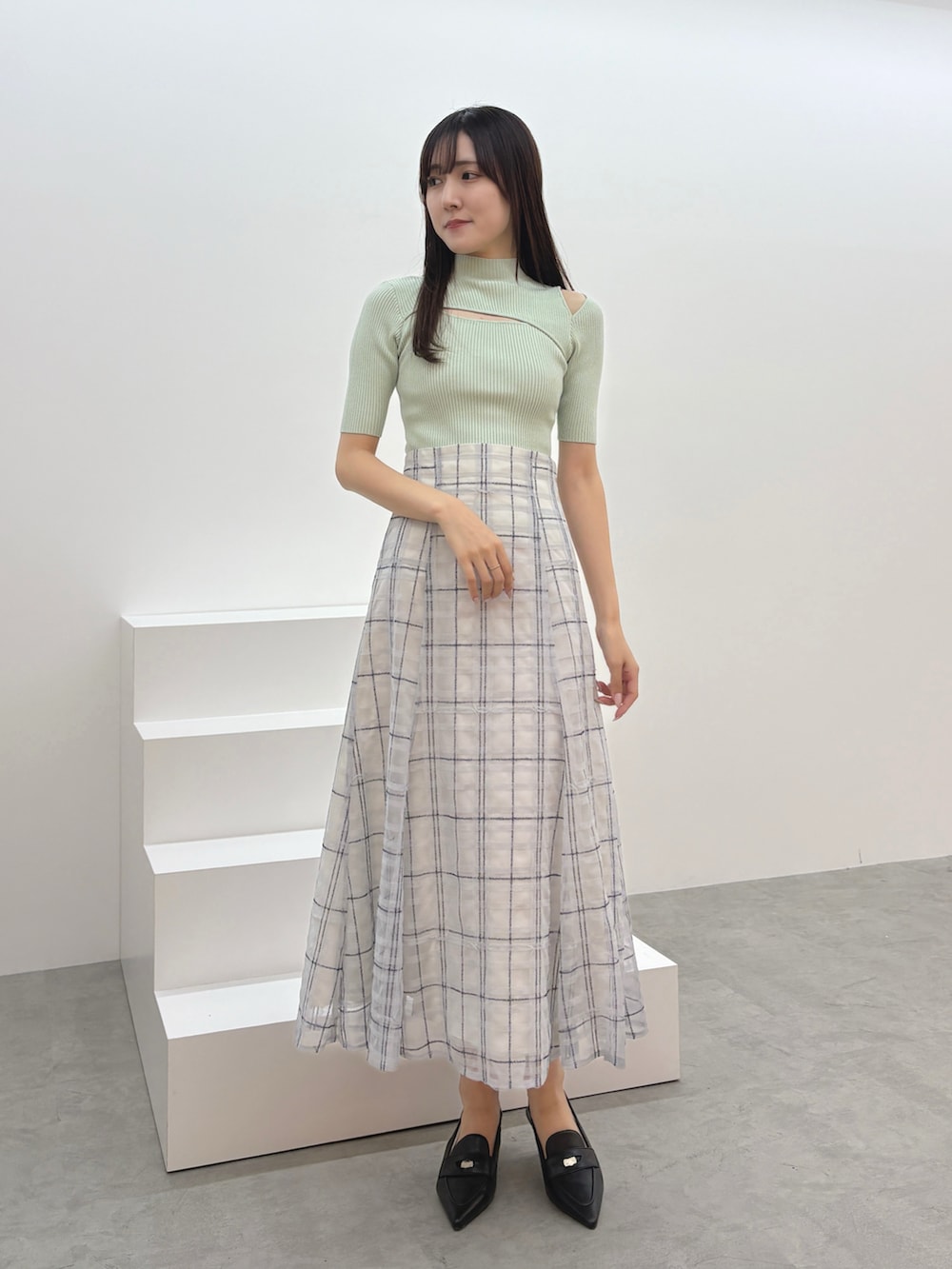 ブルー系のスカート、グリーン系のニット/セーター、ブラック系のパンプスを着用したレディースの夏コーディネートの2枚目の写真