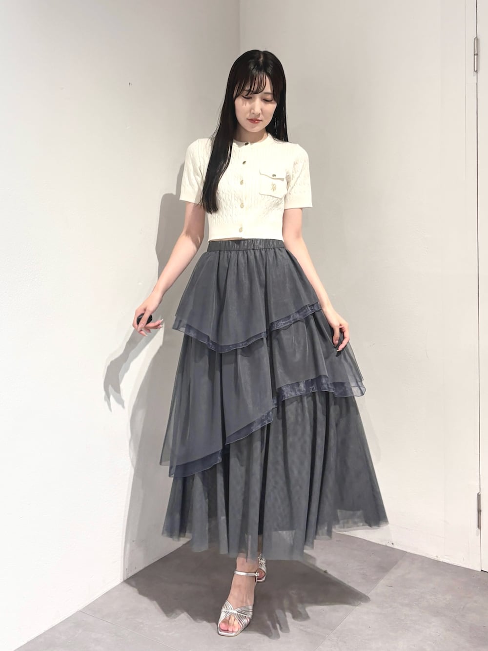 グレー系のスカート、ホワイト系のカーディガン/ボレロ、シルバー系のサンダルを着用したレディースの夏コーディネートの2枚目の写真