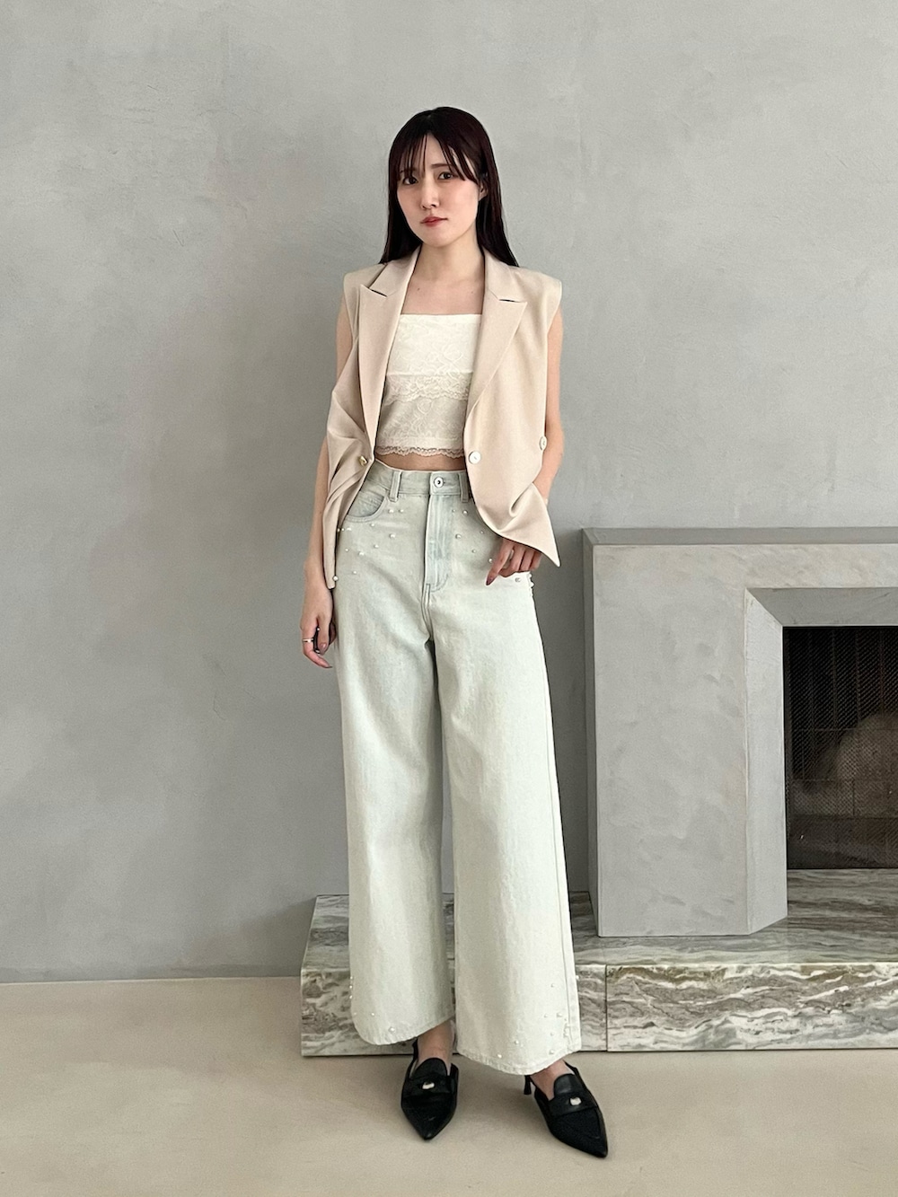 ブラック系のパンプス、ベージュ系のベスト、ブルー系のデニムパンツを着用したレディースの春コーディネートの2枚目の写真