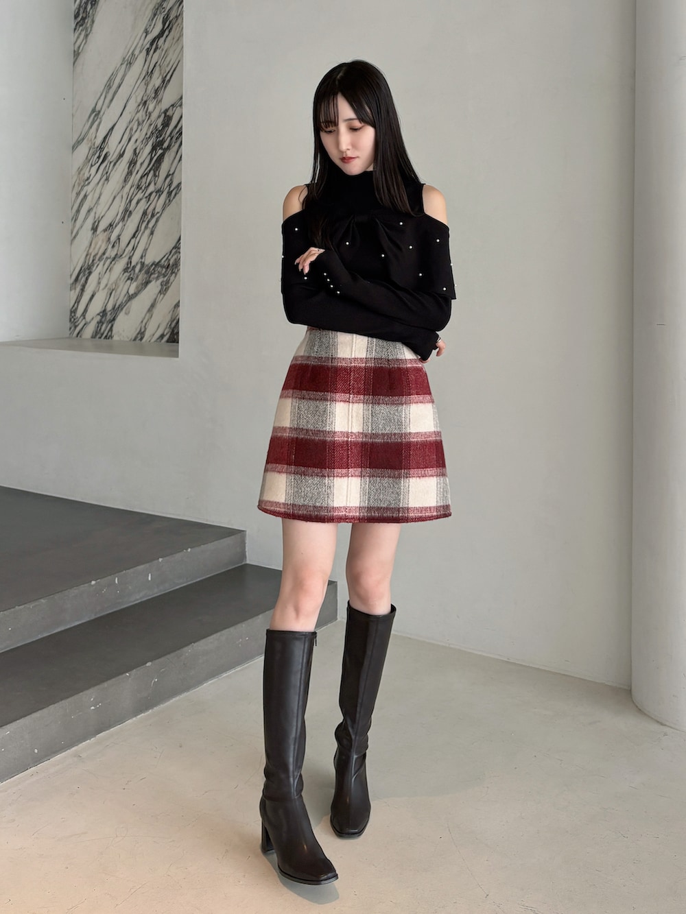 ブラック系のニット/セーター、レッド系のスカート、ブラウン系のブーツを着用したレディースの冬コーディネートの2枚目の写真