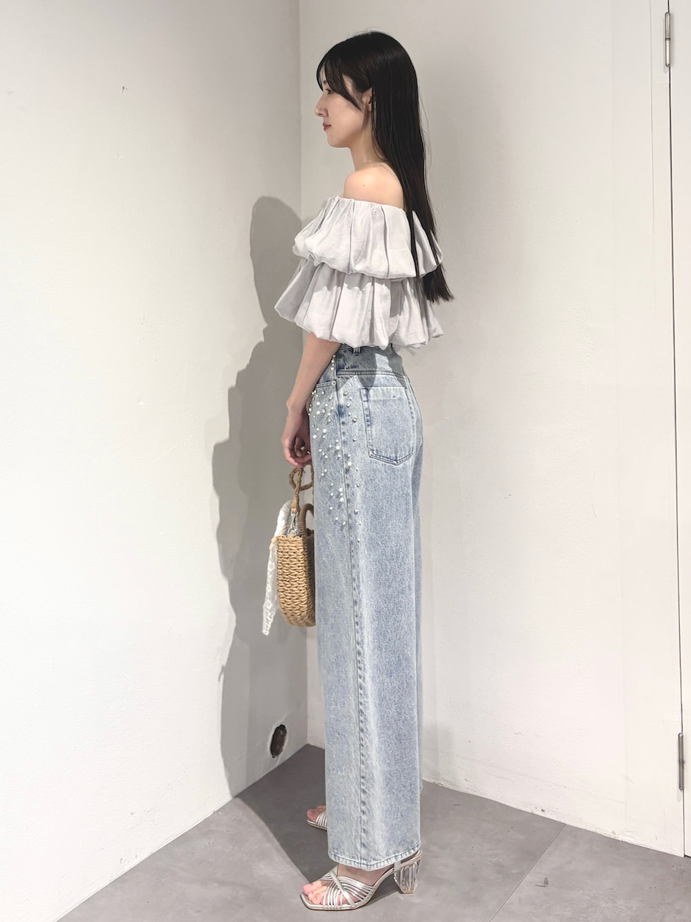 ブルー系のデニムパンツ、ベージュ系のハンドバッグ、シルバー系のサンダルを着用したレディースの夏コーディネートの3枚目の写真