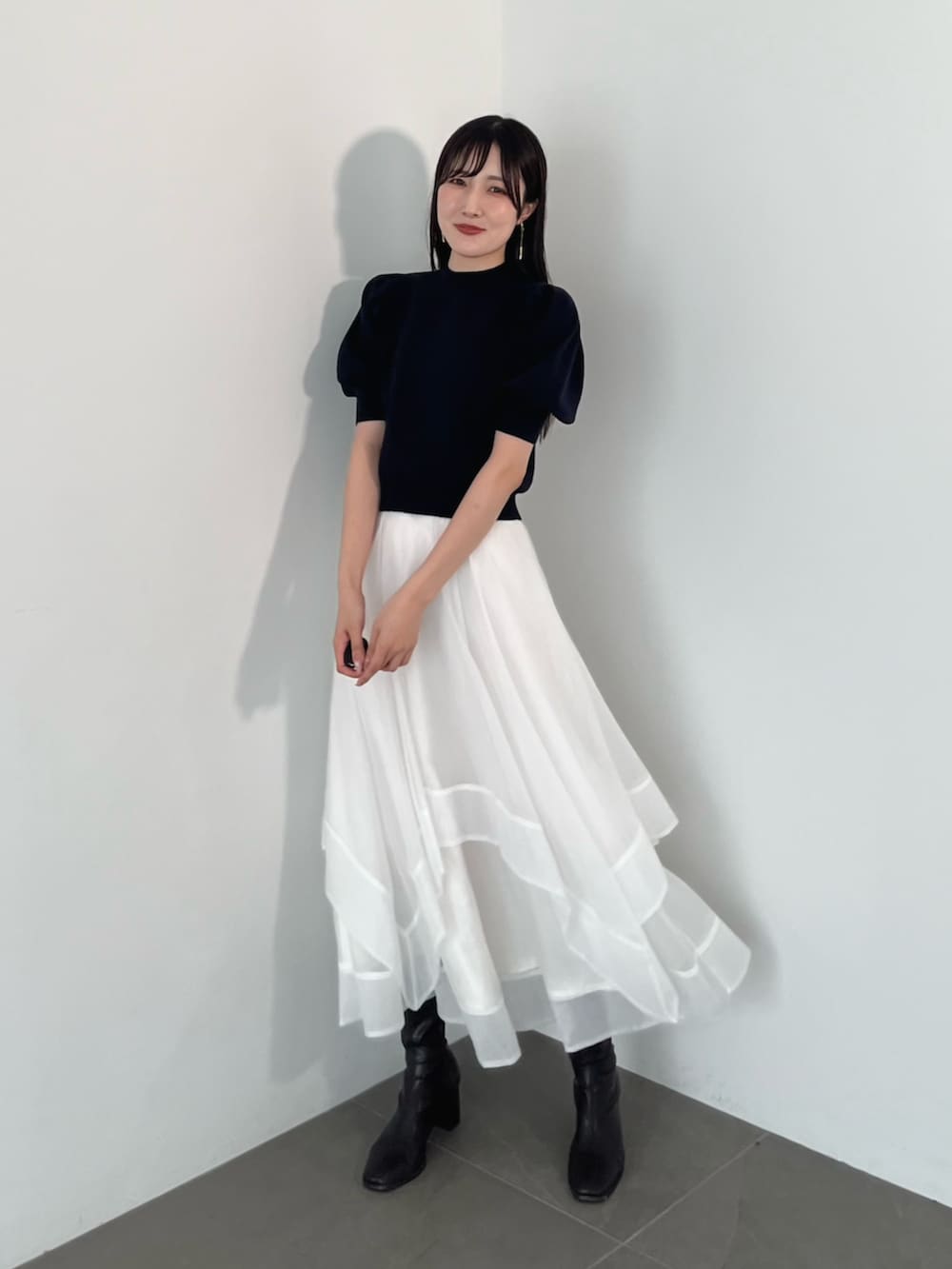 ブラック系のブーツ、ブルー系のニット/セーター、ホワイト系のスカートを着用したレディースの夏コーディネートの2枚目の写真