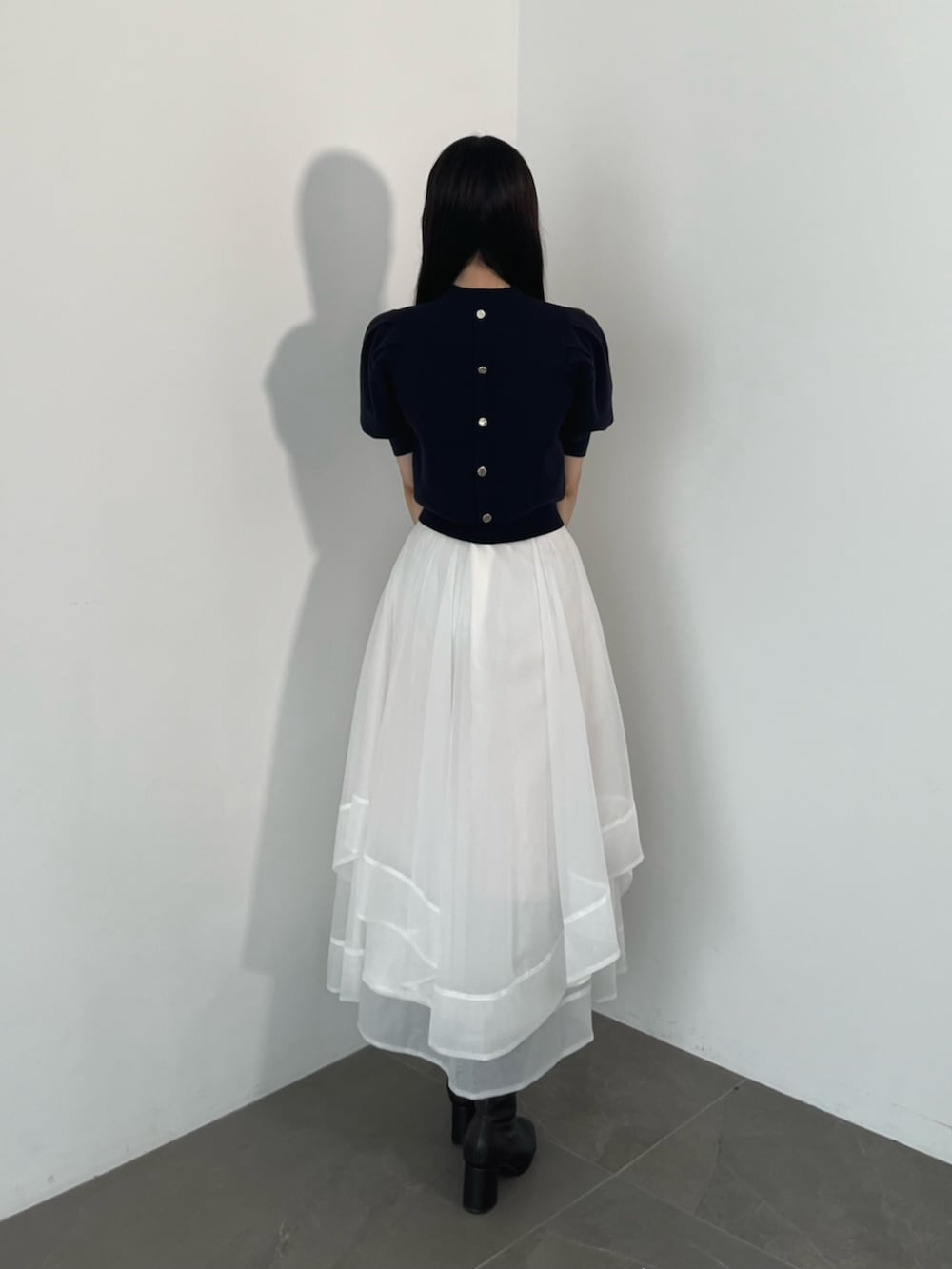 ブラック系のブーツ、ブルー系のニット/セーター、ホワイト系のスカートを着用したレディースの夏コーディネートの5枚目の写真