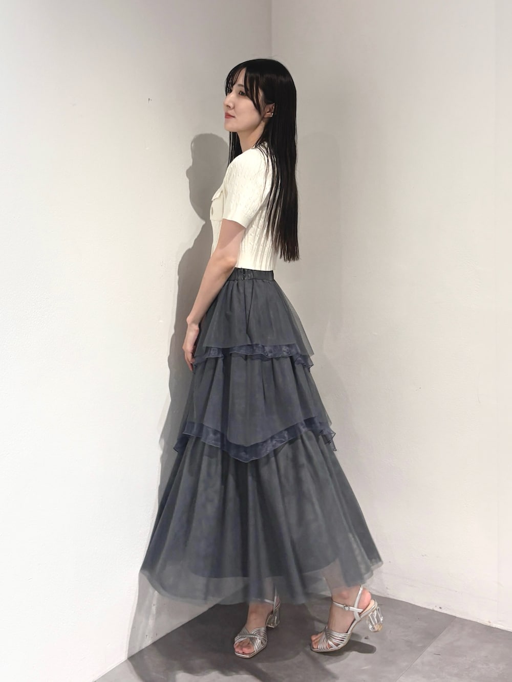 グレー系のスカート、ホワイト系のカーディガン/ボレロ、シルバー系のサンダルを着用したレディースの夏コーディネートの3枚目の写真