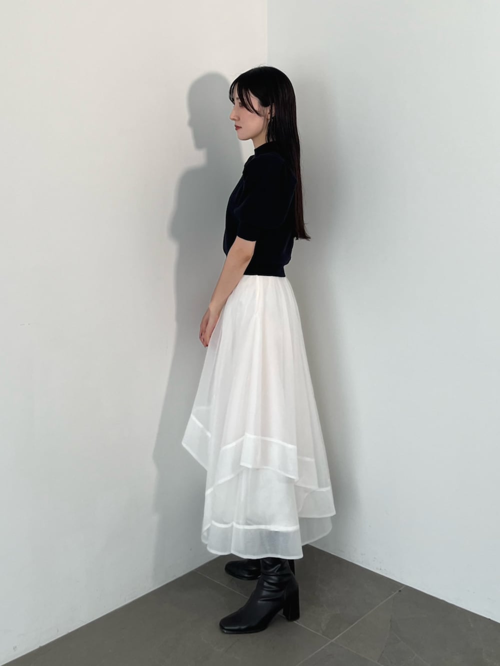 ブラック系のブーツ、ブルー系のニット/セーター、ホワイト系のスカートを着用したレディースの夏コーディネートの4枚目の写真