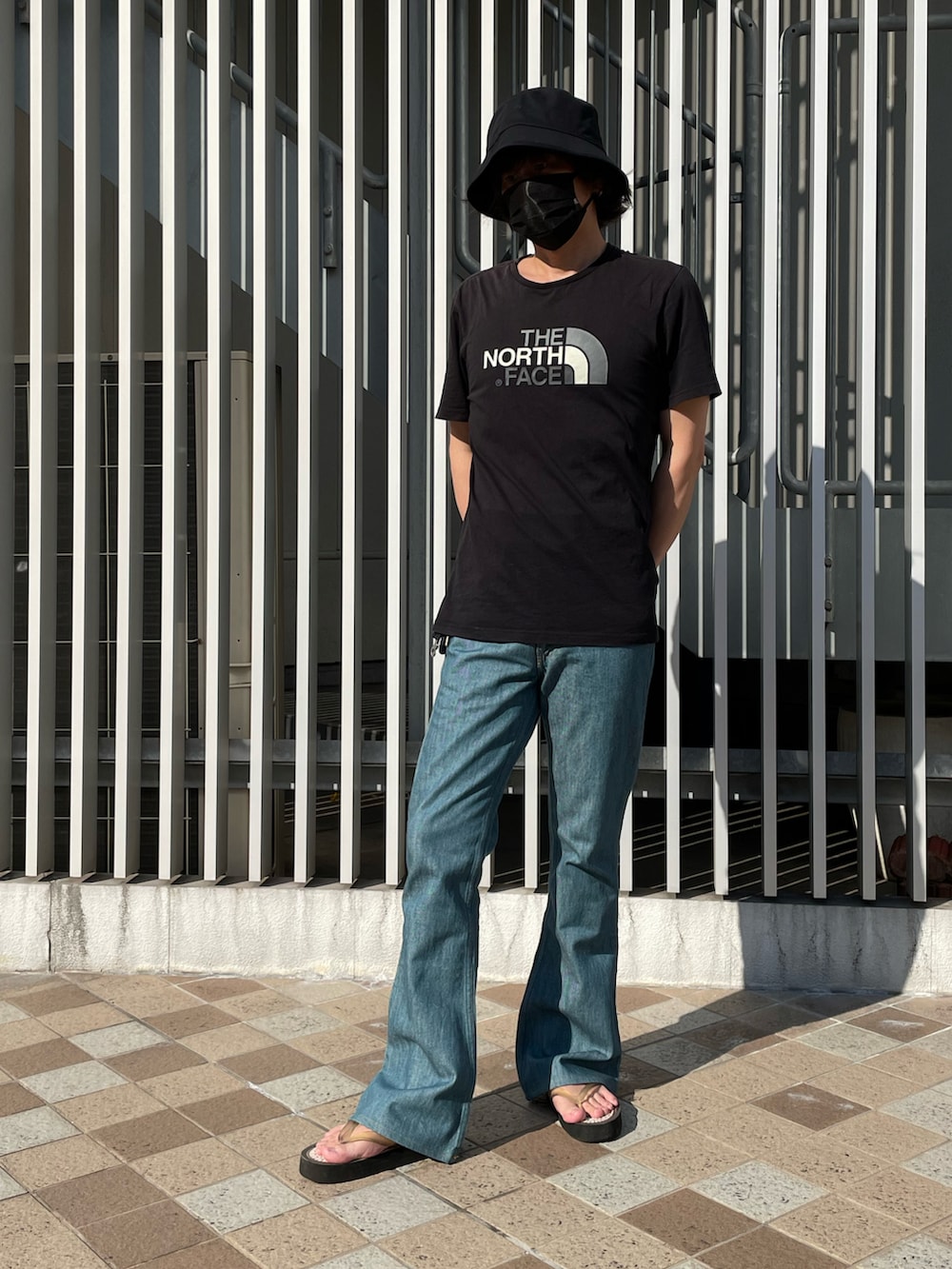 ブラック系のTシャツ/カットソー、ブルー系のデニムパンツ、ホワイト系のサンダルを着用したメンズの夏コーディネートの2枚目の写真