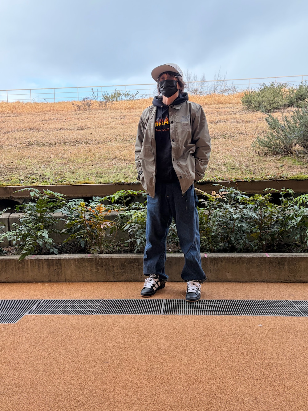 ブラック系のパーカー、グリーン系のナイロンジャケット、ブルー系のサロペット/オーバーオールを着用したメンズの春コーディネートの2枚目の写真