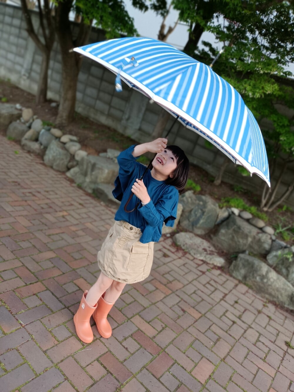 ブルー系のTシャツ/カットソー、ベージュ系のスカート、オレンジ系のレインシューズを着用したキッズの夏コーディネートの2枚目の写真