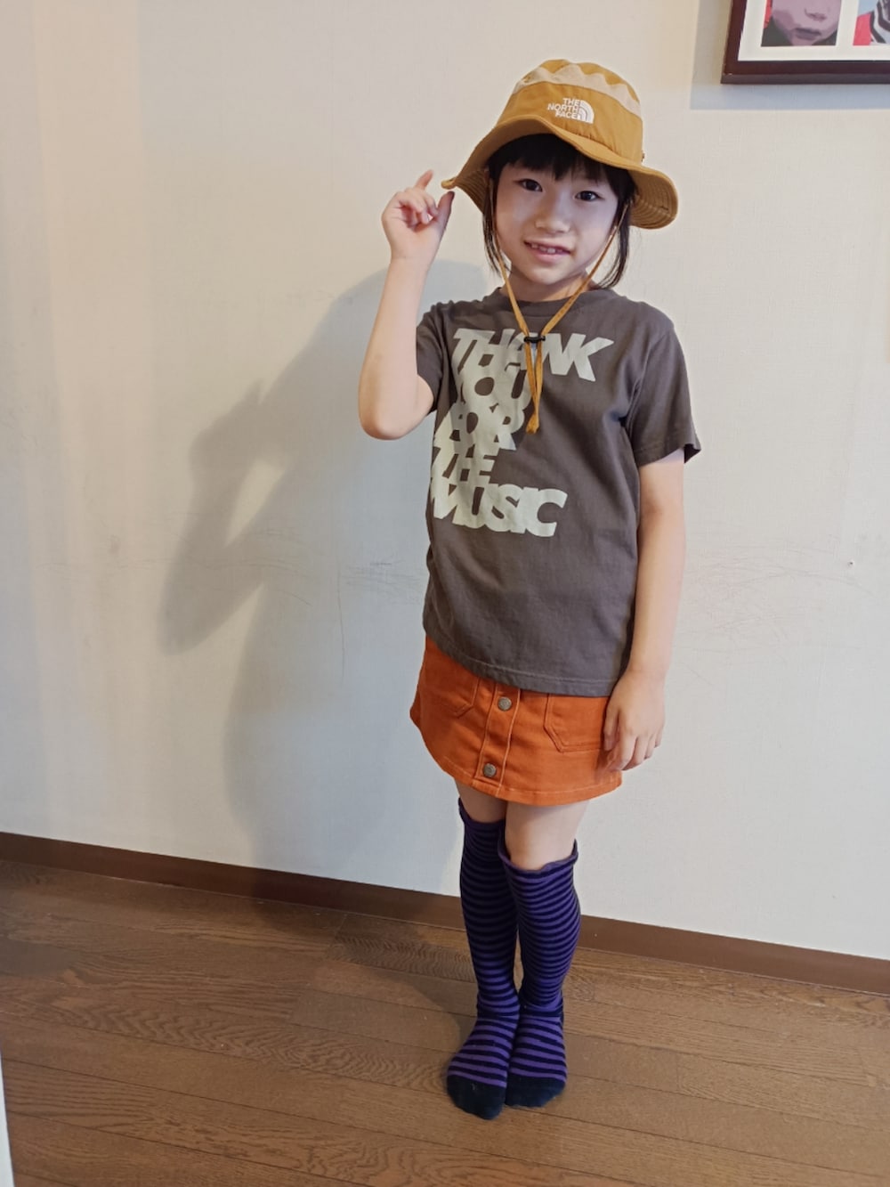 ブラック系のTシャツ/カットソー、オレンジ系のスカート、ゴールド系のハットを着用したキッズの夏コーディネートの2枚目の写真