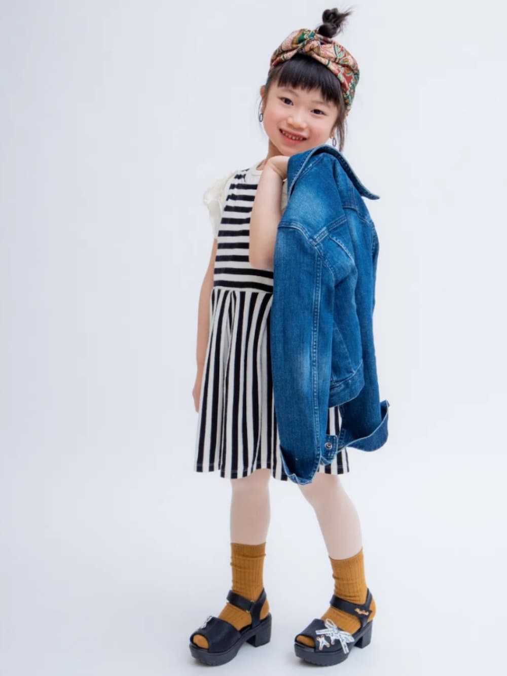 ブルー系のデニムジャケット、ブラック系のワンピース、ブラック系のサンダルを着用したキッズの秋コーディネートの2枚目の写真
