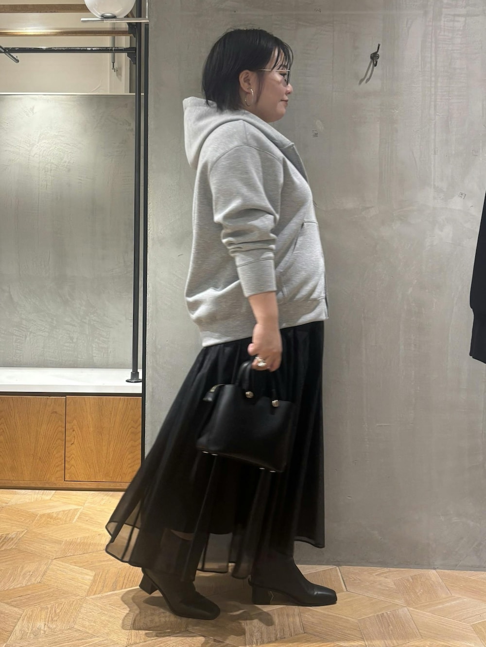 グレー系のパーカー、ブラック系のスカート、ブラウン系のブーツを着用したレディースの秋コーディネートの2枚目の写真