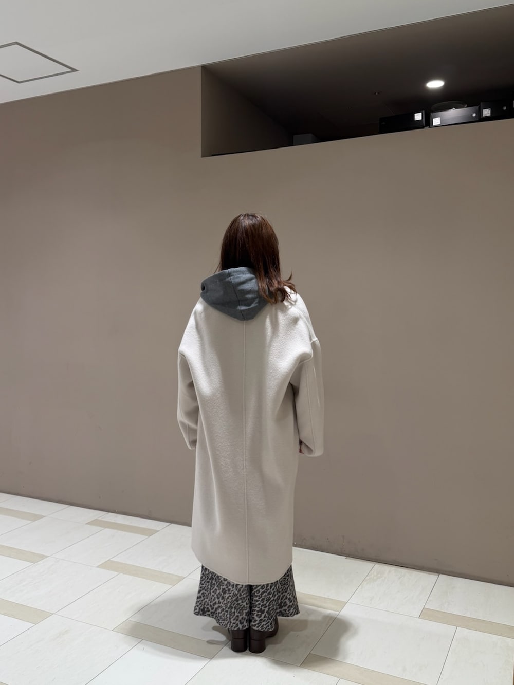 グレー系のパーカー、ベージュ系のチェスターコート、ブラウン系のスカートを着用したレディースの秋コーディネートの3枚目の写真