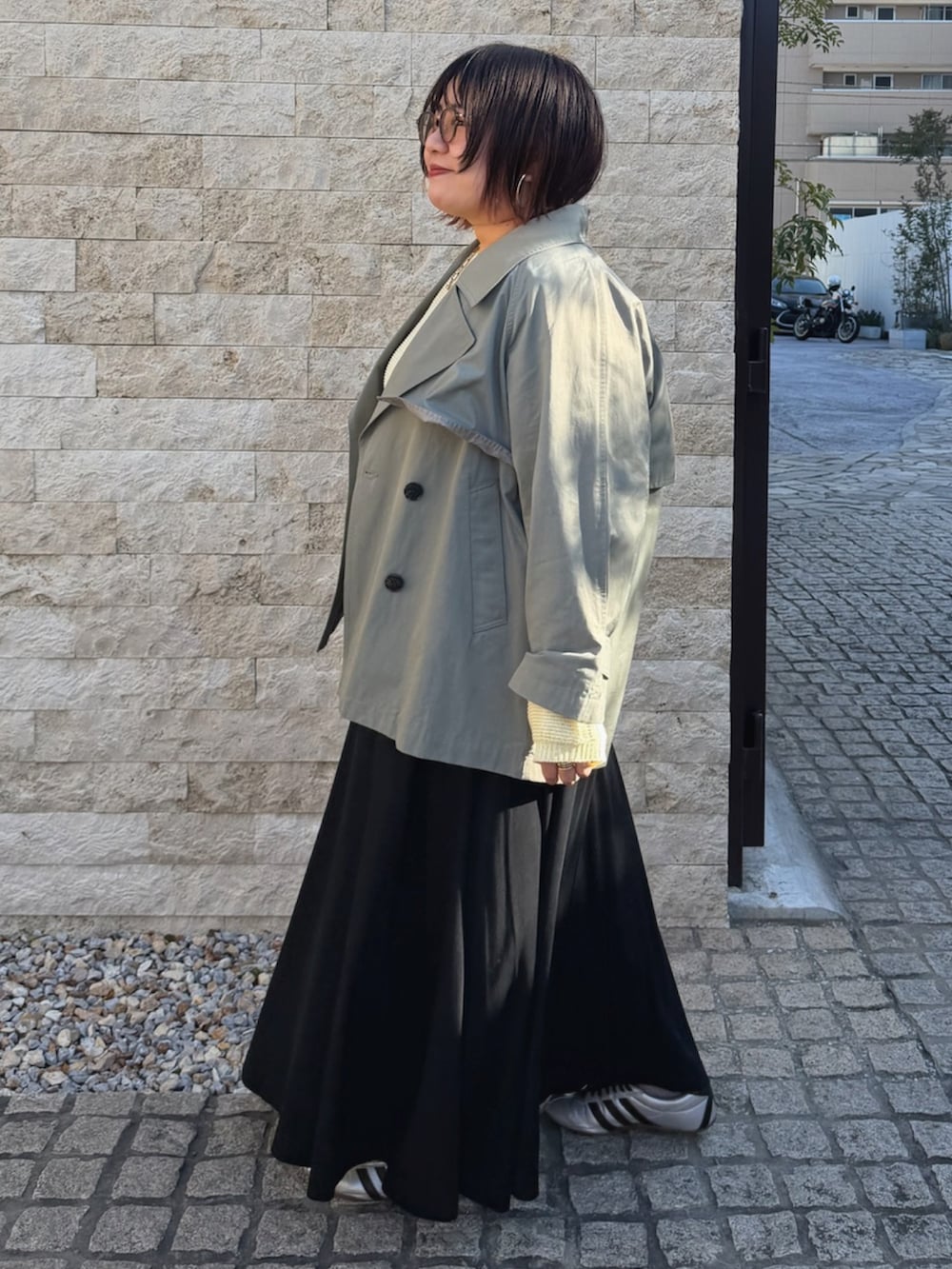 イエロー系のニット/セーター、グリーン系のトレンチコートを着用したレディースの春コーディネートの2枚目の写真