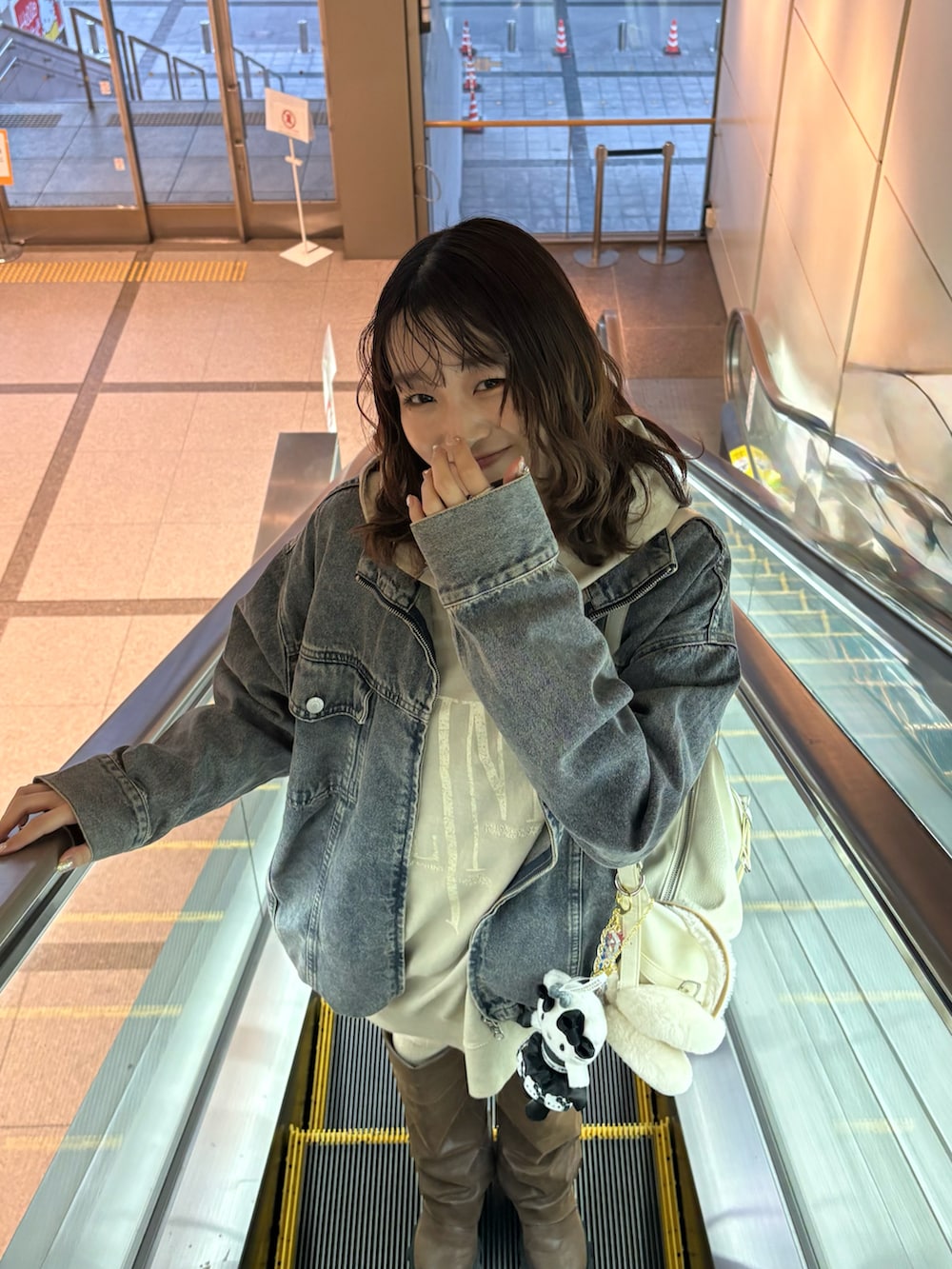 ベージュ系のパーカー、ブルー系のデニムジャケット、ホワイト系のショルダーバッグを着用したレディースの冬コーディネートの2枚目の写真