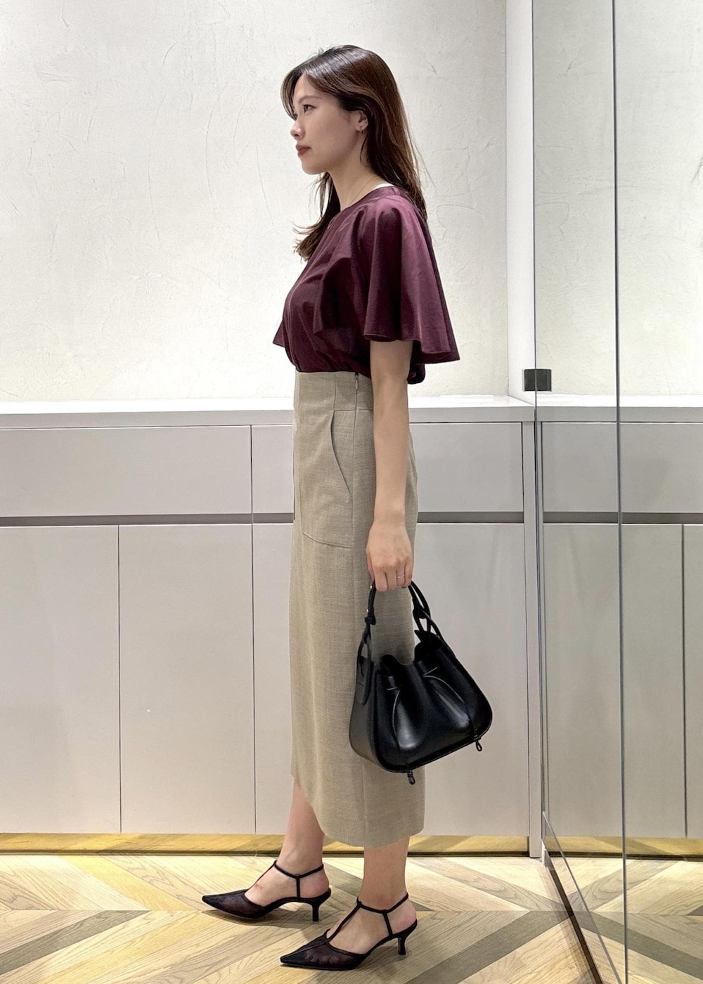 ブラック系のショルダーバッグ、ブラック系のパンプス、ベージュ系のスカートを着用したレディースの夏コーディネートの2枚目の写真