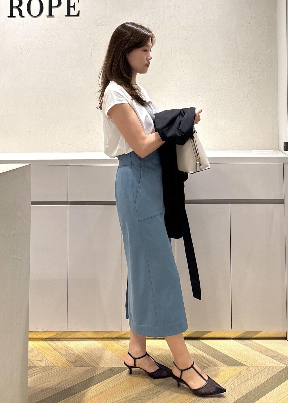 グレー系のハンドバッグ、ブラック系のパンプス、ブラック系のテーラードジャケットを着用したレディースの夏コーディネートの5枚目の写真