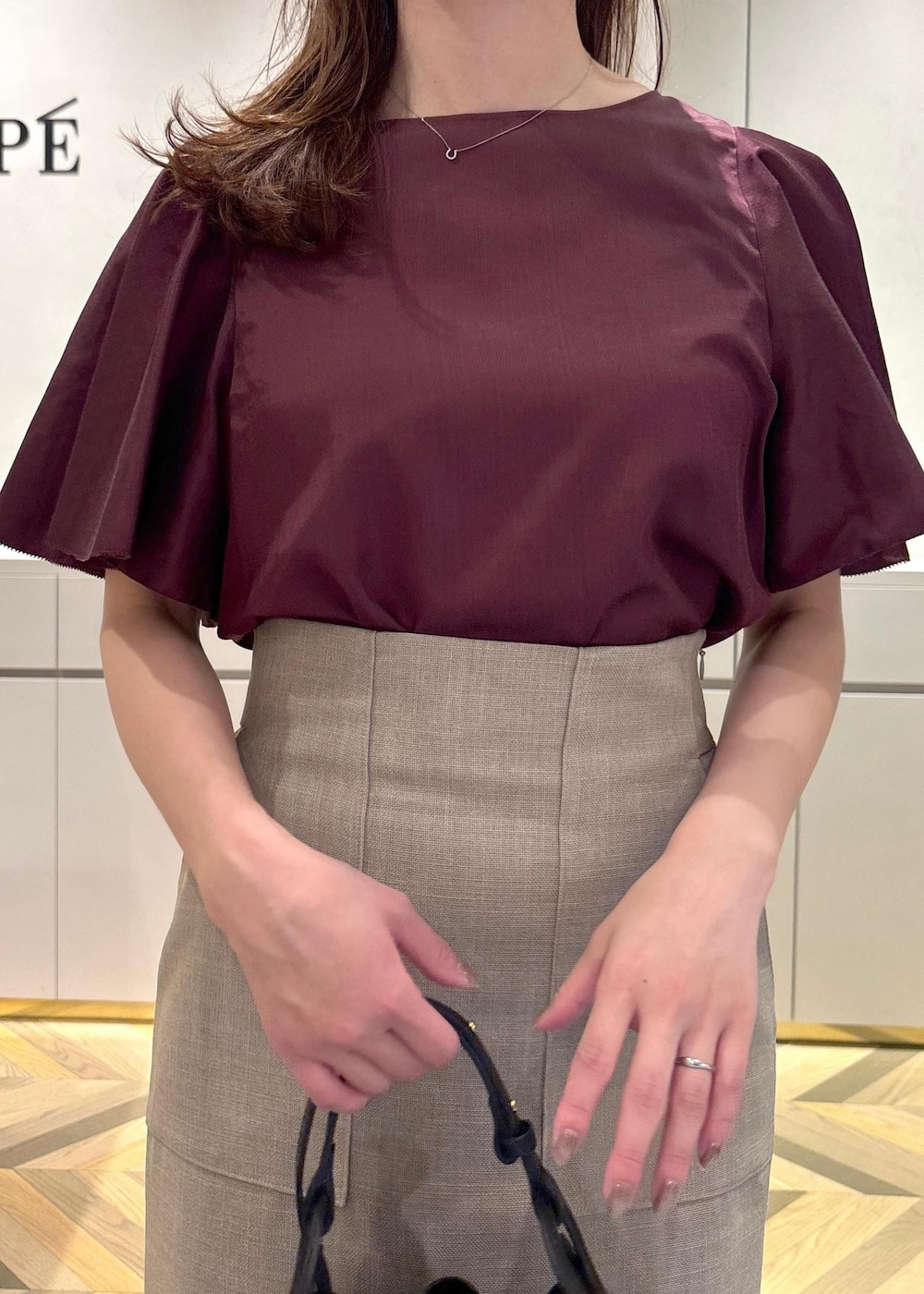 ブラック系のショルダーバッグ、ブラック系のパンプス、ベージュ系のスカートを着用したレディースの夏コーディネートの4枚目の写真