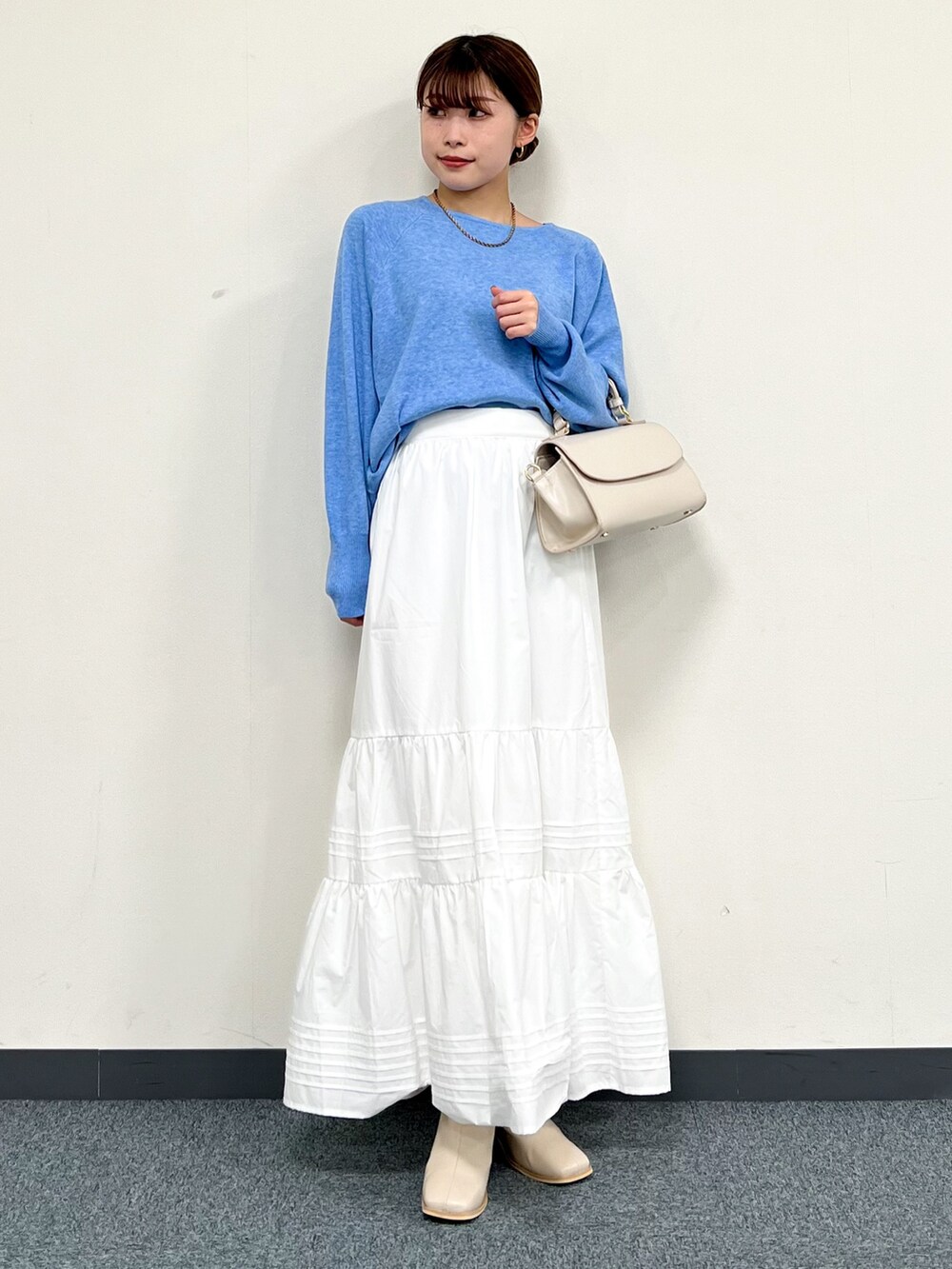 ブルー系のニット/セーター、ベージュ系のハンドバッグ、ベージュ系のノーカラーコートを着用したレディースの冬コーディネートの5枚目の写真