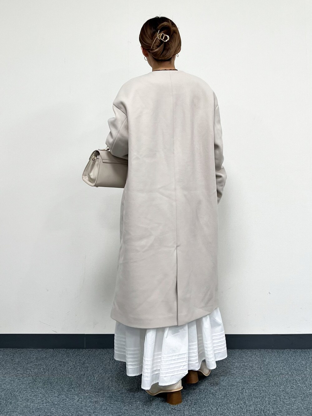 ブルー系のニット/セーター、ベージュ系のハンドバッグ、ベージュ系のノーカラーコートを着用したレディースの冬コーディネートの3枚目の写真