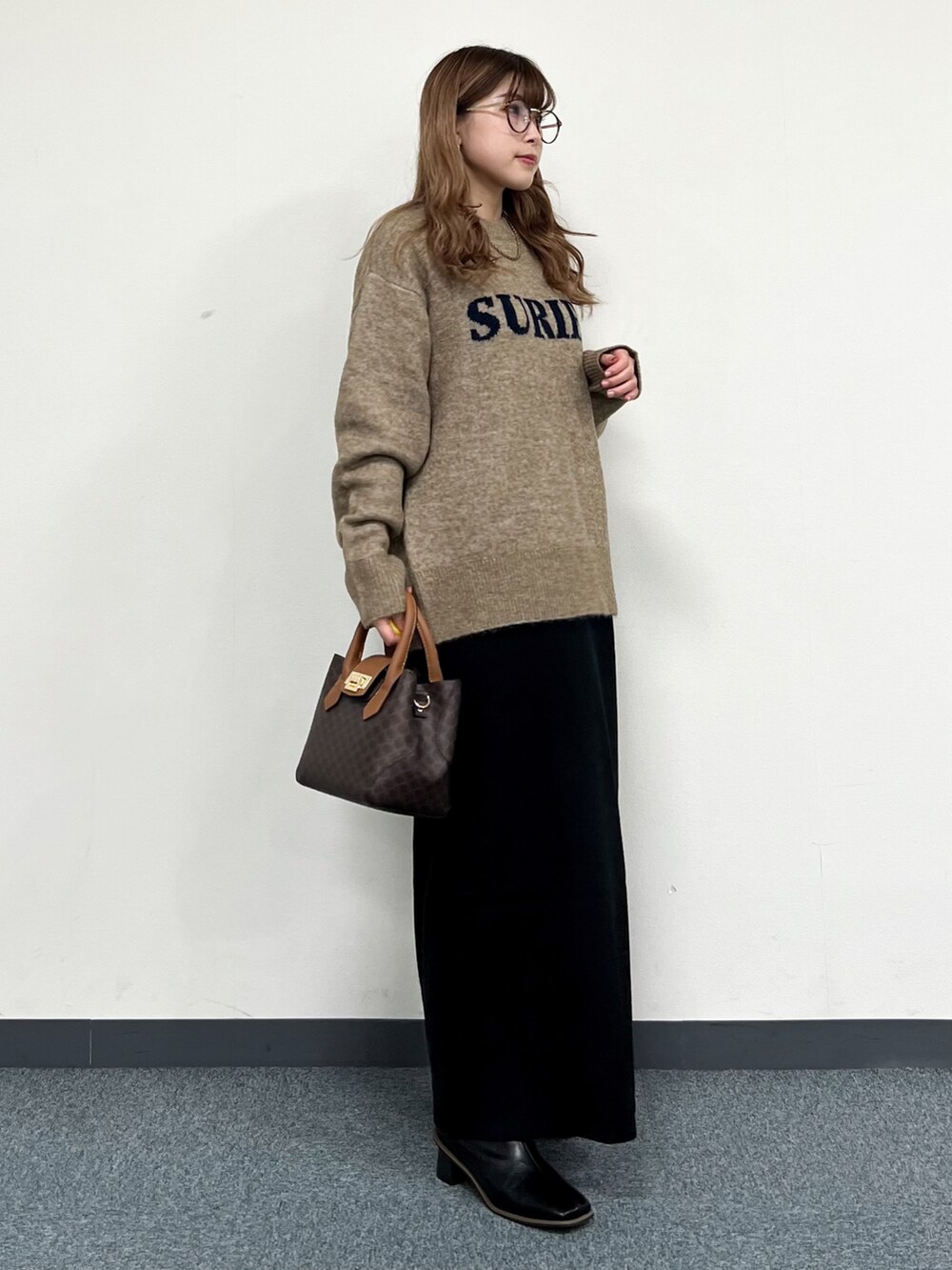 ブラウン系のショルダーバッグ、ベージュ系のニット/セーター、ブラック系のワンピースを着用したレディースの冬コーディネートの2枚目の写真