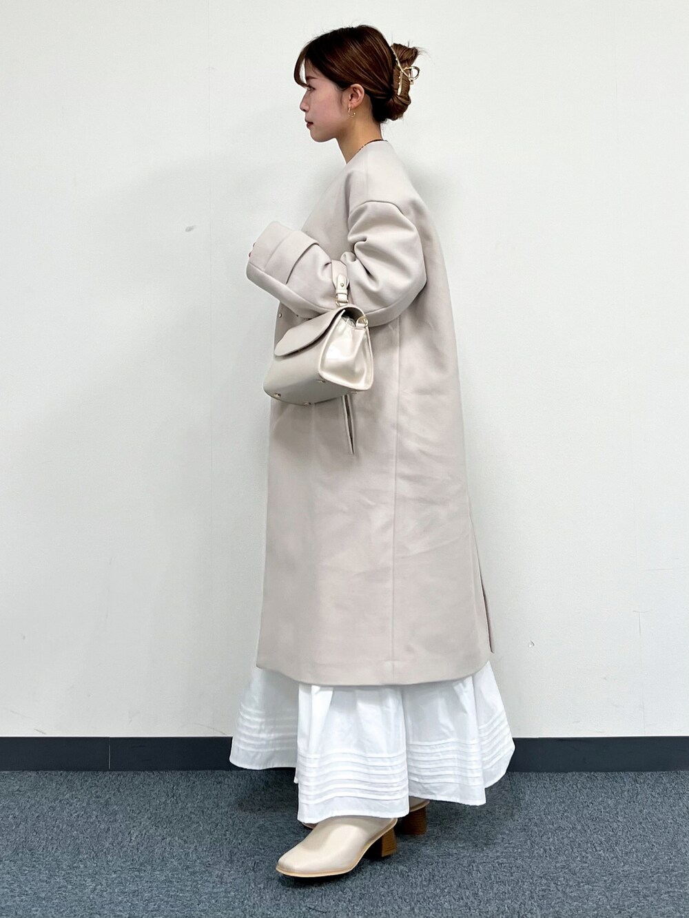 ブルー系のニット/セーター、ベージュ系のハンドバッグ、ベージュ系のノーカラーコートを着用したレディースの冬コーディネートの4枚目の写真