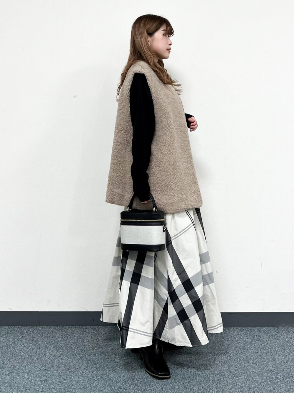 ブラック系のニット/セーター、ベージュ系のベスト、ホワイト系のスカートを着用したレディースの冬コーディネートの2枚目の写真