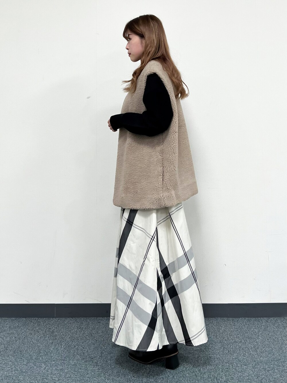 ブラック系のニット/セーター、ベージュ系のベスト、ホワイト系のスカートを着用したレディースの冬コーディネートの4枚目の写真
