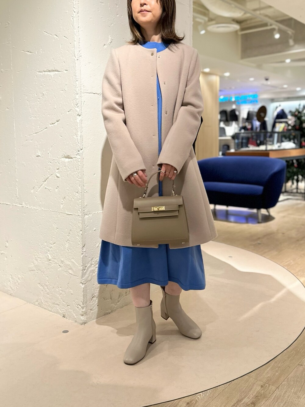 ベージュ系のショルダーバッグ、ホワイト系のブーツ、ブルー系のワンピースを着用したレディースの冬コーディネートの2枚目の写真