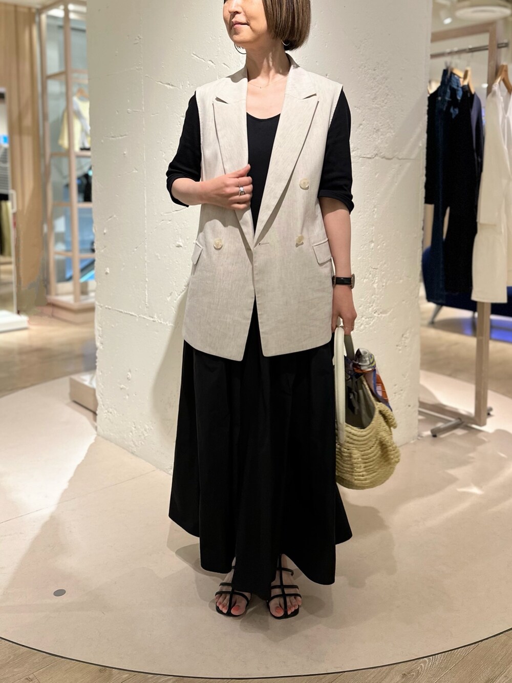 ブラック系のワンピース、ベージュ系のベスト、ベージュ系のかごバッグを着用したレディースの春コーディネートの2枚目の写真
