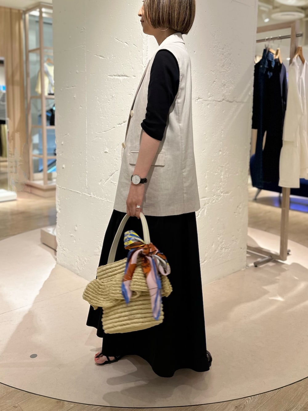 ブラック系のワンピース、ベージュ系のベスト、ベージュ系のかごバッグを着用したレディースの春コーディネートの3枚目の写真