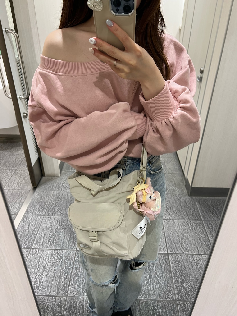 ピンク系のスウェット、ベージュ系のバッグ、ブルー系のデニムパンツを着用したレディースの夏コーディネートの2枚目の写真