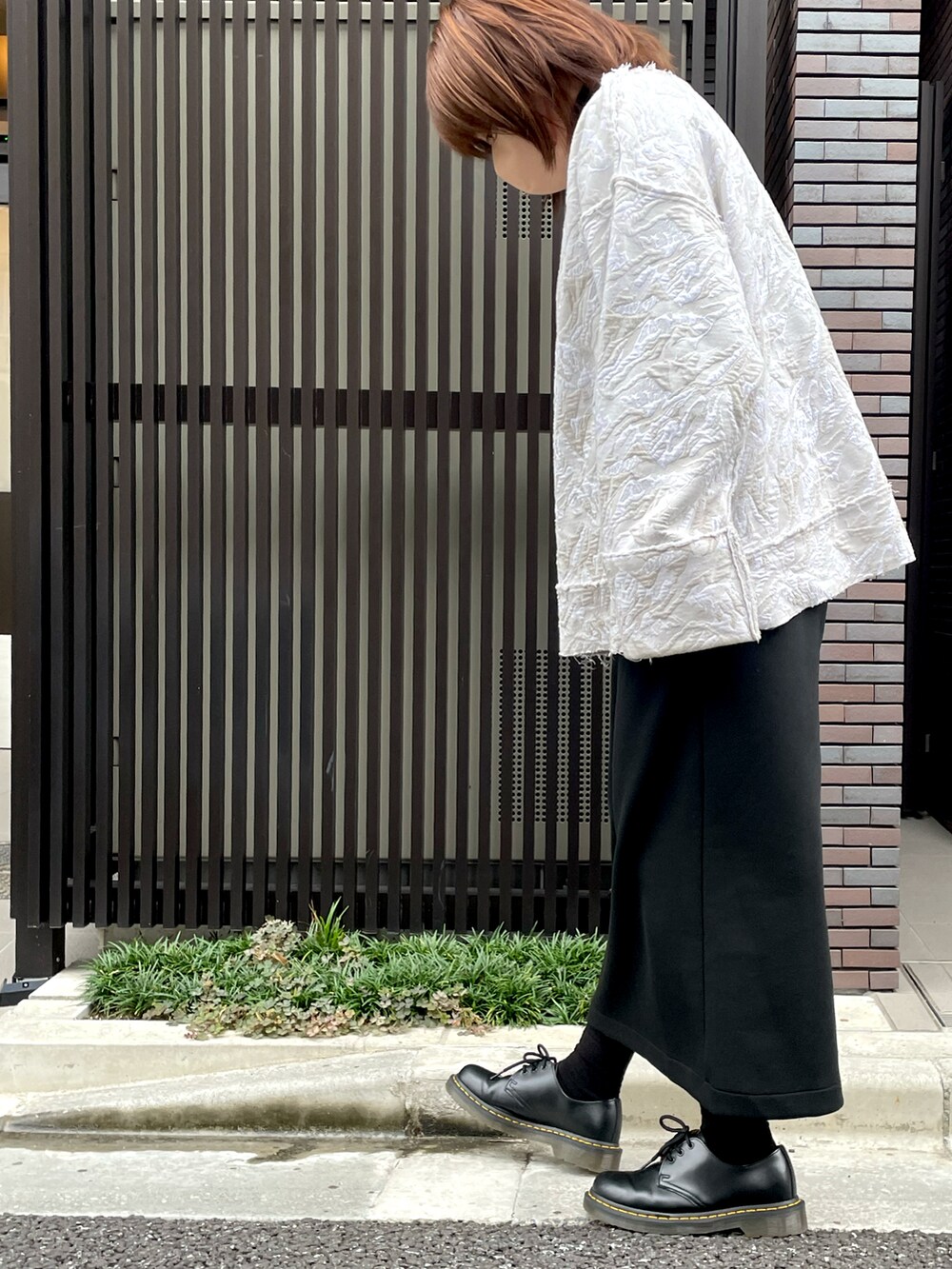 ホワイト系のトップス、ブラック系のスカート、ブラック系のブーツを着用したレディースの秋コーディネートの2枚目の写真