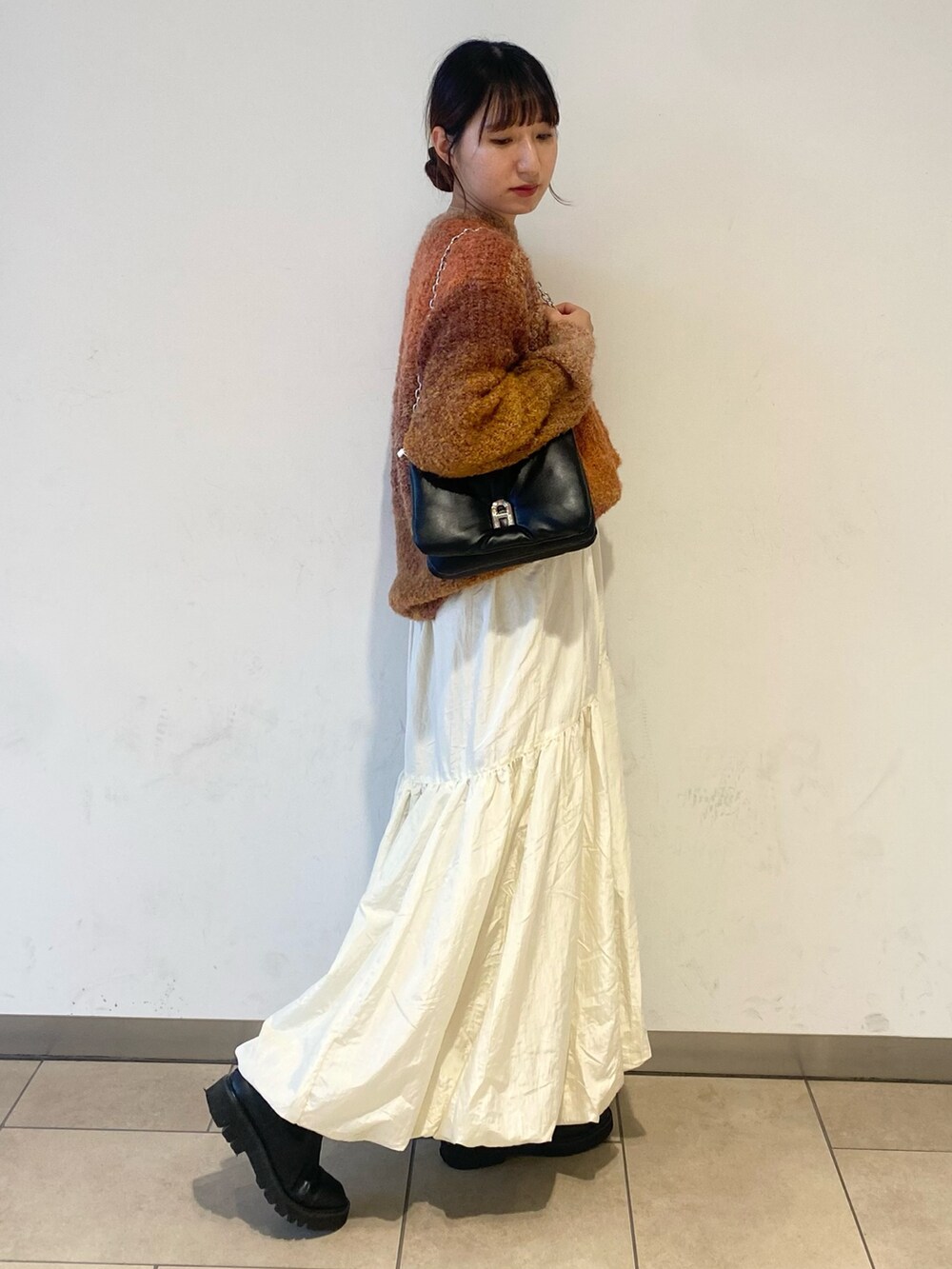 ホワイト系のスカート、オレンジ系のニット/セーター、ブラック系のブーツを着用したレディースの秋コーディネートの2枚目の写真