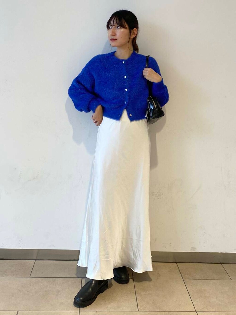 ブルー系のカーディガン/ボレロ、ブラック系のブーツ、ホワイト系のスカートを着用したレディースの冬コーディネートの2枚目の写真