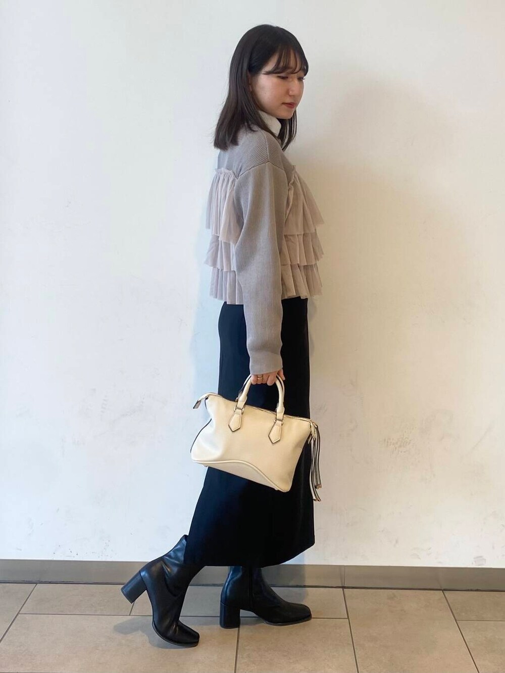 ホワイト系のボストンバッグ、ブラック系のブーツ、ベージュ系のニット/セーターを着用したレディースの冬コーディネートの2枚目の写真