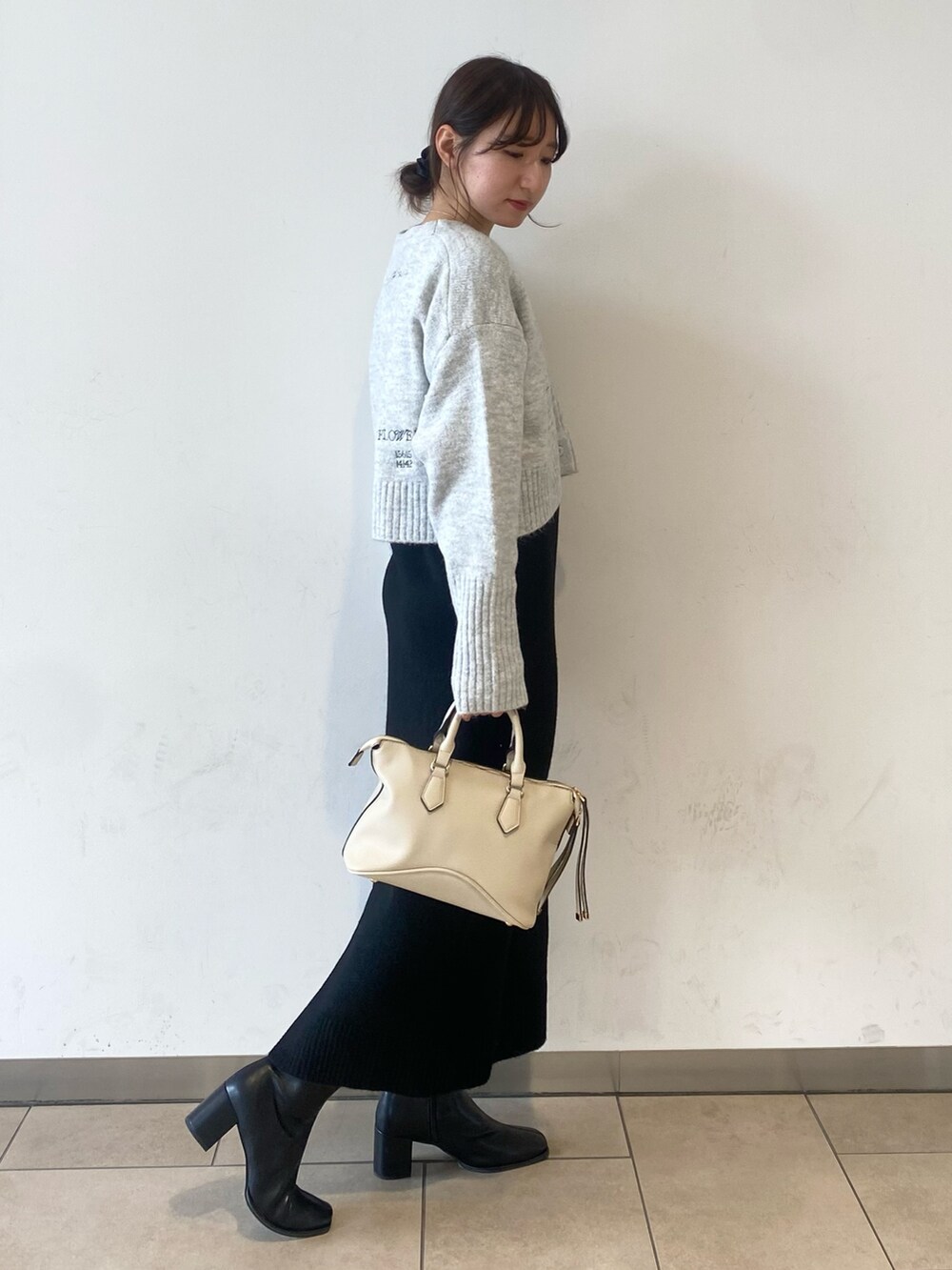 ホワイト系のボストンバッグ、ブラック系のブーツ、グレー系のワンピースを着用したレディースの冬コーディネートの2枚目の写真